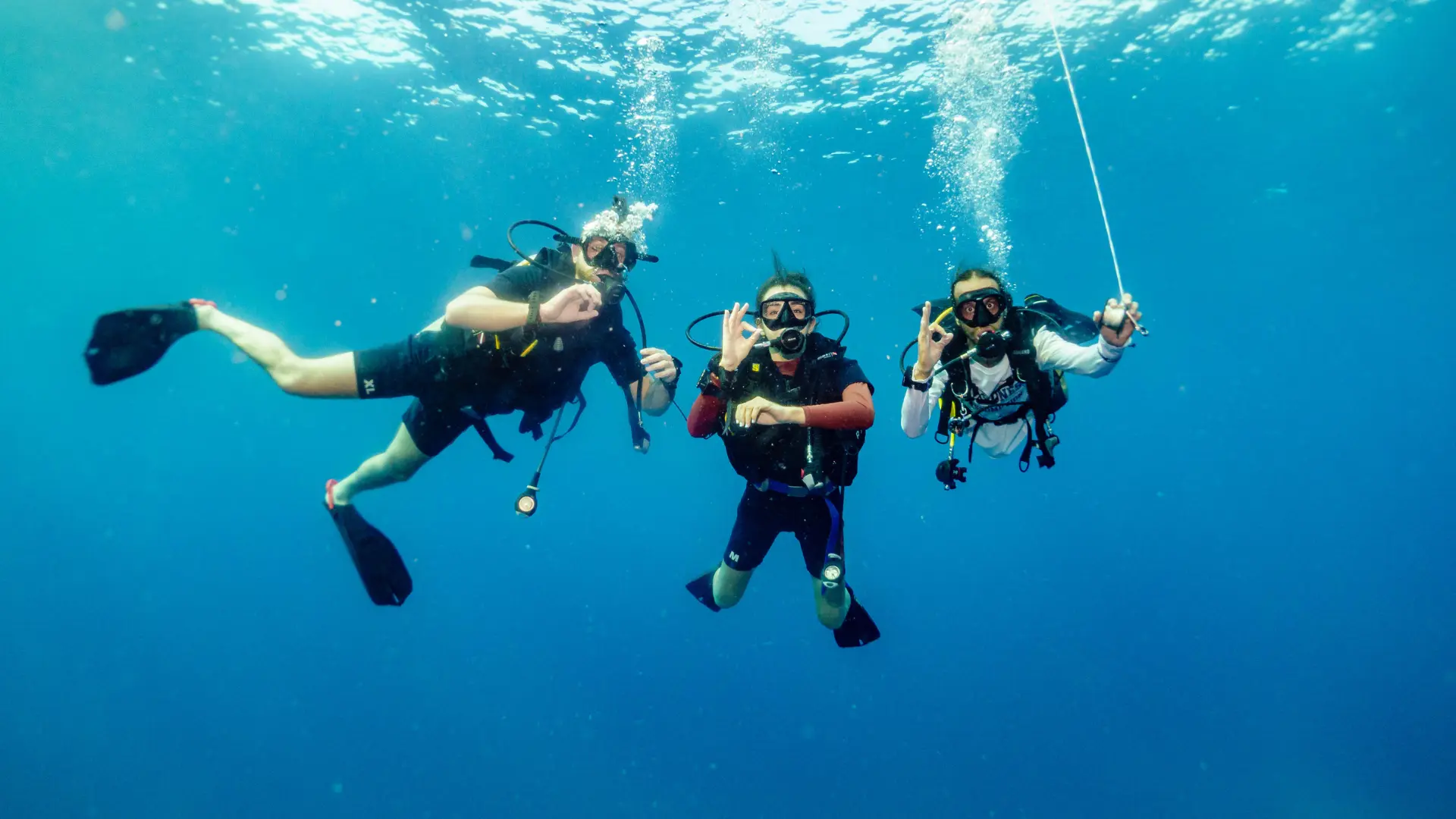 Three scuba divers are swimming underwater together during a guided dive in clear water.
